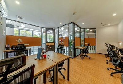 Bright open-plan workspace with wooden desks and black ergonomic chairs.
