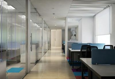 Bright office corridor featuring glass partitions and open-plan workstations with blue privacy screens.