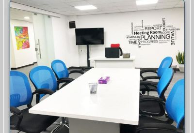 Professional meeting room with a large white table, blue mesh chairs, and wall-mounted screen.