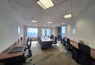 Large shared office space with multiple long wooden desks and black ergonomic chairs.