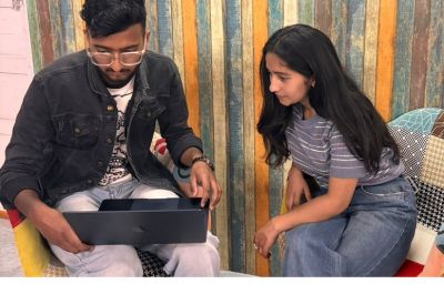 Two people working together on a laptop against a colorful wood-paneled wall.