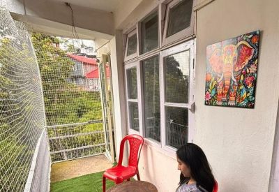 Outdoor balcony seating area with a red chair, small table, and vibrant elephant artwork.