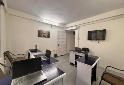 Bright coworking area with workstations, white desks, and a wall-mounted television.