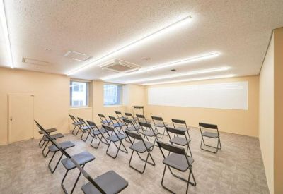 Bright seminar room with rows of black folding chairs facing a large white wall.