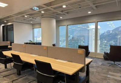 Bright open-plan workspace with wooden desks, ergonomic chairs, and large windows.