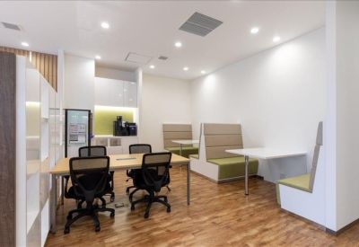 Modern breakout area with wooden floors, communal desks, and green-upholstered booth seating.