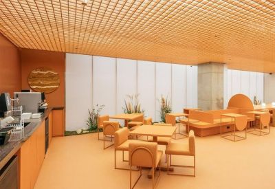 Coworking café area with orange seating, wooden tables, and a textured grid ceiling.