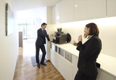 Bright breakroom with a coffee station and white cabinetry over wood flooring.