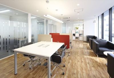 Spacious coworking area with long white tables and various seating zones.