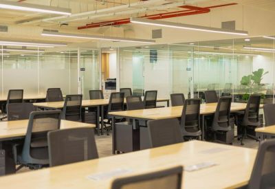 Open-plan workspace featuring rows of wooden desks and black ergonomic chairs.