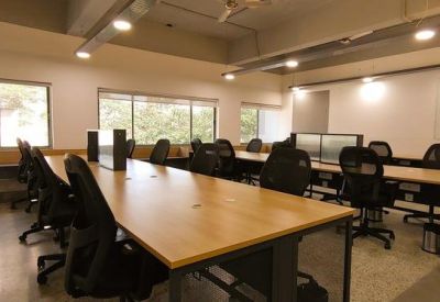 Large open-plan workspace featuring long wooden communal desks and ergonomic black mesh chairs.