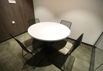 Small breakout room featuring a white circular table and black mesh chairs against a dark wood wall.