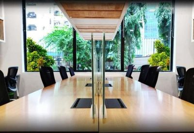 Bright open-plan office with long wooden desks and views of greenery.