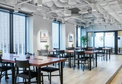 Open-plan coworking office with rows of wooden desks and industrial-style ceilings.