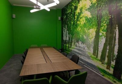 Meeting room with a long wooden table, green chairs, and a vibrant forest-themed wall mural.