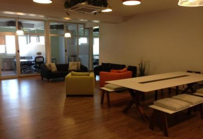 Open-plan coworking area featuring a large white table and breakout seating with orange and lime accents.