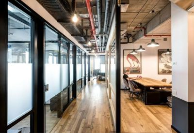 Long office corridor with glass partitions and exposed overhead piping.