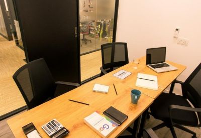 Wooden meeting table with laptops and stationery in a glass-partitioned room.