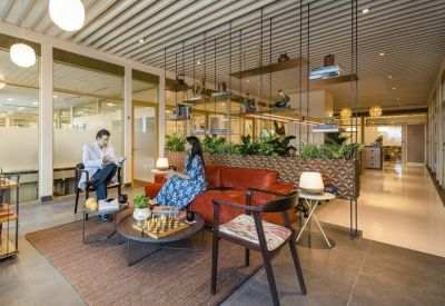 Bright communal lounge with a leather sofa, patterned rug, and hanging plants.