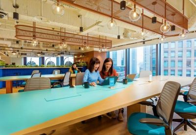 Open-plan workspace featuring a large teal desk, modern lighting, and city skyline views.