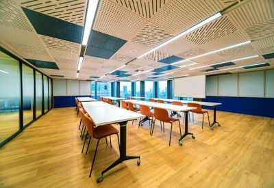 Bright training or meeting room with rows of white desks, orange chairs, and city views.