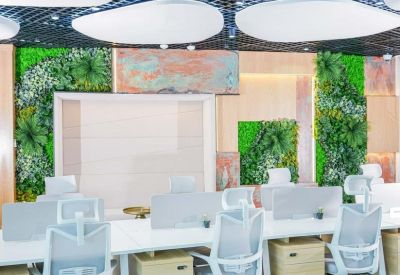 Modern open-plan office with white desks, ergonomic chairs, and vibrant green plant walls.