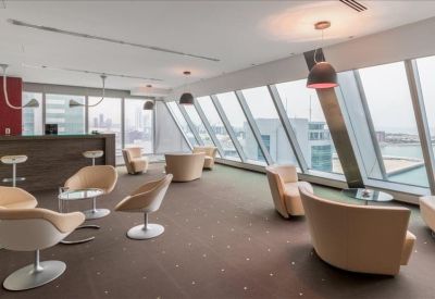Stylish breakout lounge with modern bucket chairs and a bar area set against slanted windows.