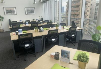 Modern open-plan workspace featuring rows of desks, ergonomic chairs, and large windows.