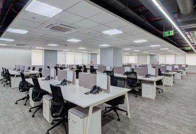Spacious open-plan workspace with rows of white desks and ergonomic black chairs under bright panel lighting.
