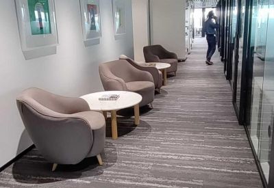 Modern corridor lounge featuring plush grey armchairs and a decorative grid ceiling.