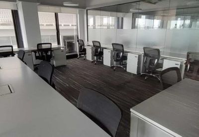 Bright open-plan office space with rows of white desks and ergonomic black chairs.