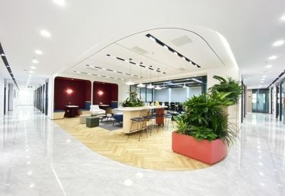 Bright, open coworking area with a central high table, greenery, and polished marble floors.