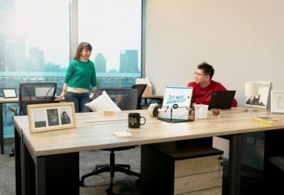Two people working at a wooden shared desk near a large window with city views.