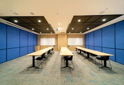 Classroom-style meeting room with blue acoustic wall panels and rows of light wood tables.