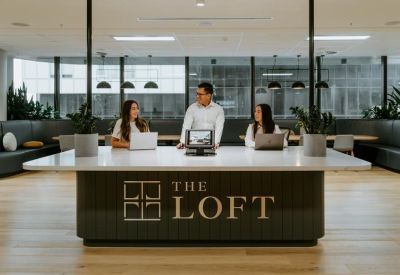 Reception area with a large front desk featuring The Loft branding and staff with laptops.