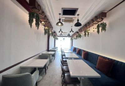Long communal dining or cafe area with white tables, blue banquette seating, and hanging plants.