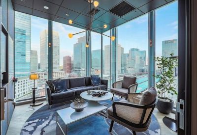 Lounge area with a dark sofa and floor-to-ceiling windows overlooking city skyscrapers.
