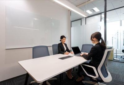 Two professionals meeting in a bright corner office with a glass partition.