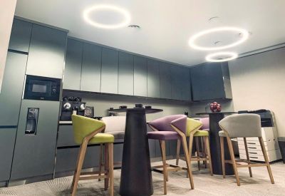 Communal kitchen area with colorful bar stools and circular overhead lighting.