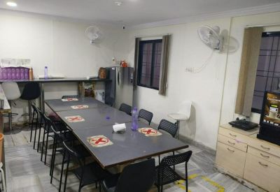 Communal dining area with a long table, black chairs, and a kitchen unit in the background.