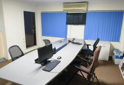 Meeting room with a long white conference table, multiple chairs, and blue window blinds.