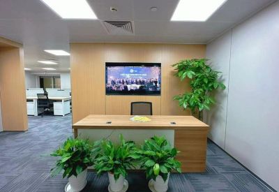 Reception desk with wood paneling, a large screen, and vibrant green potted plants.