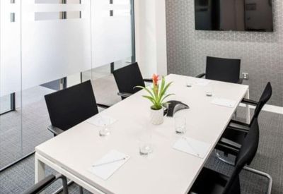 Bright modern meeting room with a white table, black chairs, and a potted plant.