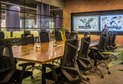 Spacious boardroom with a large wooden table, ergonomic chairs, and wall-mounted presentation screens.