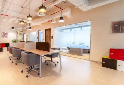 Coworking area with long desks, industrial lighting, and a view of a frosted meeting room.