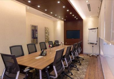 Formal boardroom with a large wooden table, black mesh chairs, and a wall-mounted screen.
