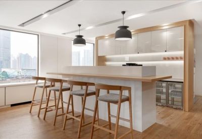 Modern kitchen and break area with high stools, a sleek white island, and warm wood accents.