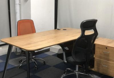 Two-person private office with wooden desk and orange mesh chair.