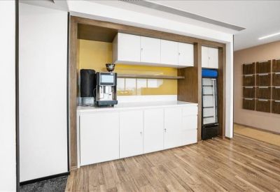 Kitchenette area featuring white cabinetry, a coffee machine, and warm wood-style flooring.