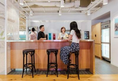 A wooden bar counter with high stools and people socializing in a bright communal area.